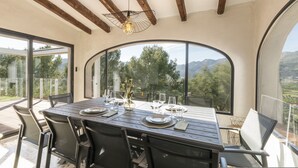 A dining area with a large table set for six, surrounded by chairs, with a view of mountains and trees through large windows. - Horizonte in El Capso (Orba)