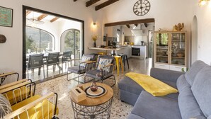 A spacious living area with a sofa, chairs, and a dining table. There is a kitchen in the background with a clock on the wall. - Horizonte in El Capso (Orba)