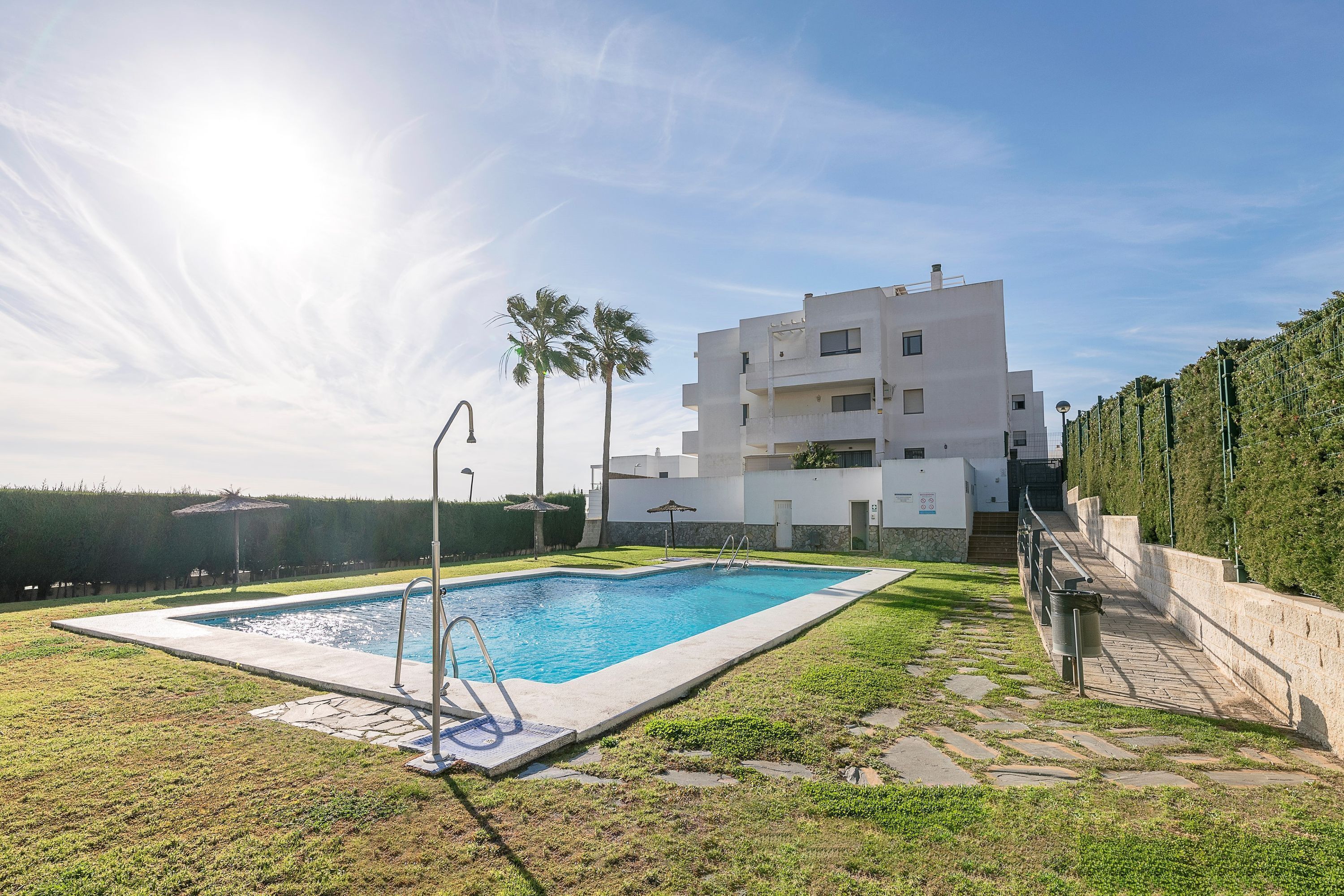 A modern building with a swimming pool, a stone pathway, and a well-maintained lawn.
