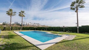 Una piscina rectangular con agua cristalina y azul, rodeada por un césped cuidado y palmeras.
