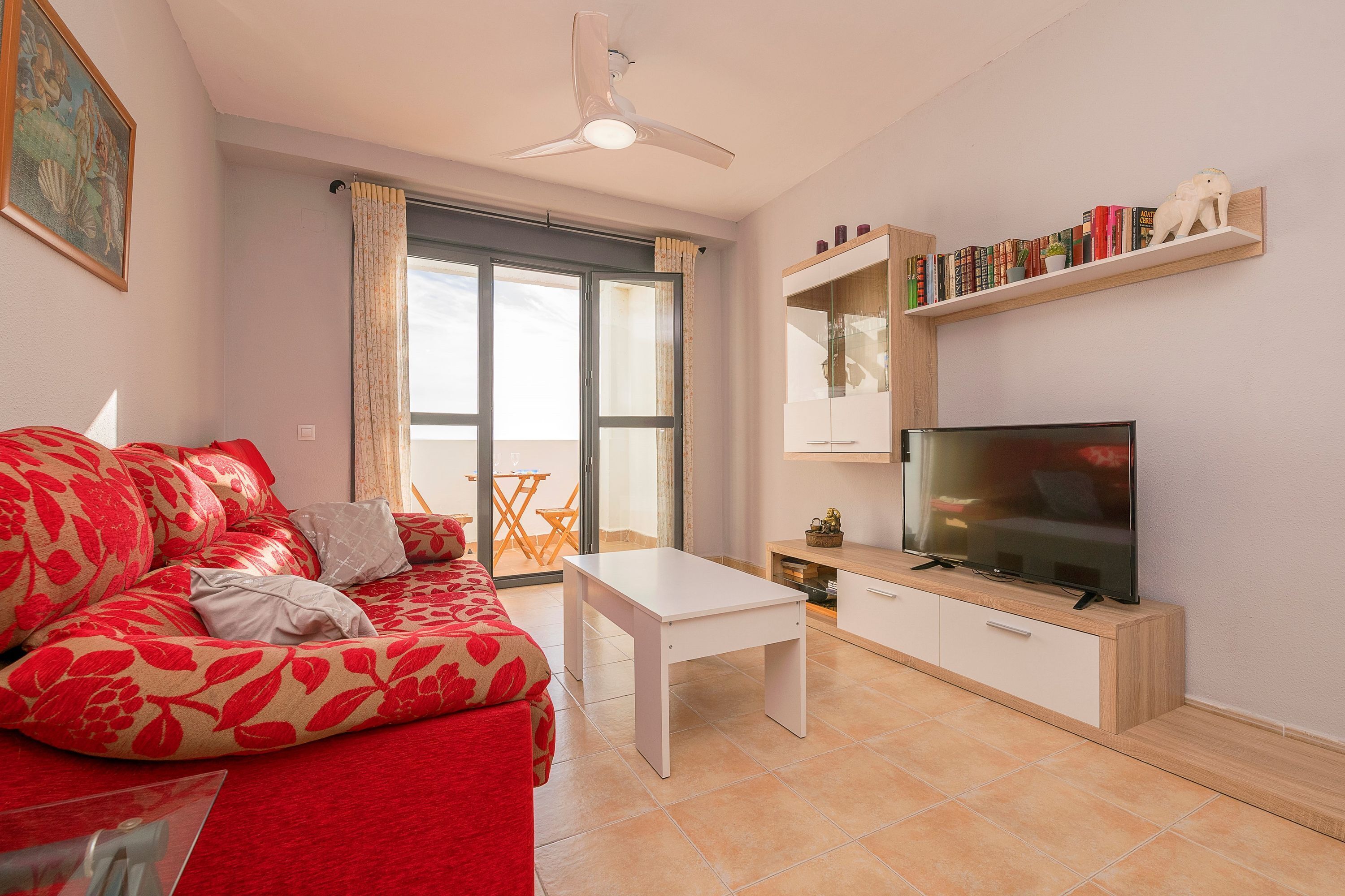 A modern living room with a red sofa, a white coffee table, a flat-screen TV, and a bookshelf.