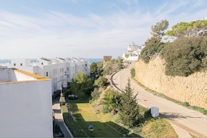 A residential area with white buildings, a curved road, and a hillside with trees.