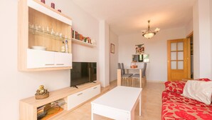 Una sala de estar con televisor, una mesa blanca, un sofá rojo y un mueble de madera con estantes.