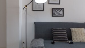 A modern living room with a grey sofa, two patterned pillows, a floor lamp, and framed artwork on the wall. - Jinetes Holidays in M Laga (Málaga)