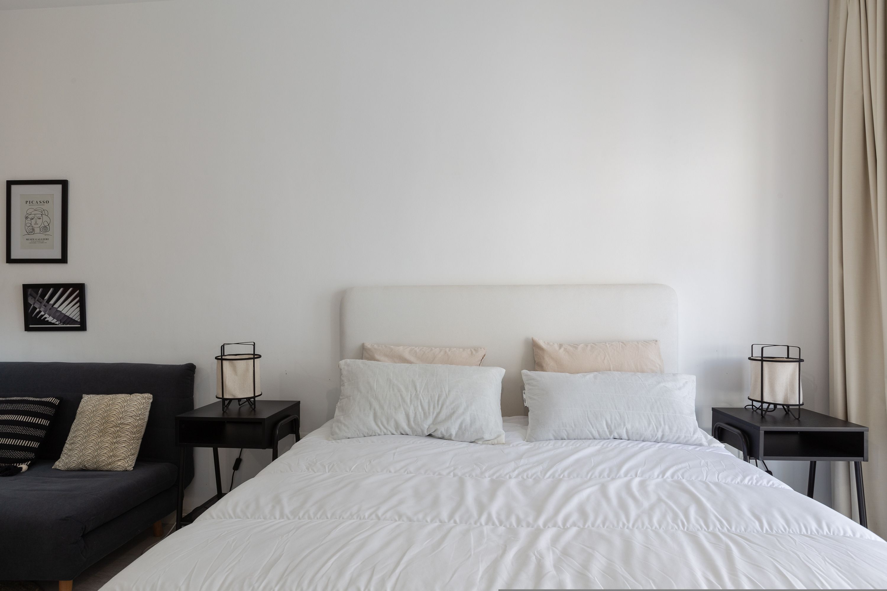 Un dormitorio ordenado con una cama, una mesita pequeña y un sofá.