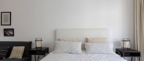 Un dormitorio ordenado con una cama, una mesita pequeña y un sofá.