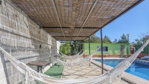 A hammock under a shaded area by a swimming pool, with a small table and a chair nearby. - La Morada Del Yayo in Guillena (Guillena)