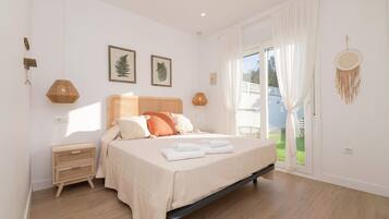 A bedroom with a bed, a bedside table, a window with curtains, and a dreamcatcher on the wall.