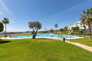 A swimming pool surrounded by a well-maintained lawn, palm trees, and a building in the background. - Lunamar in Marbella With 4 Bedrooms and 3 Bathrooms (Marbella)