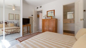 Camera da letto con un letto, un armadio in legno, una televisione e un bagno visibile attraverso una porta aperta.