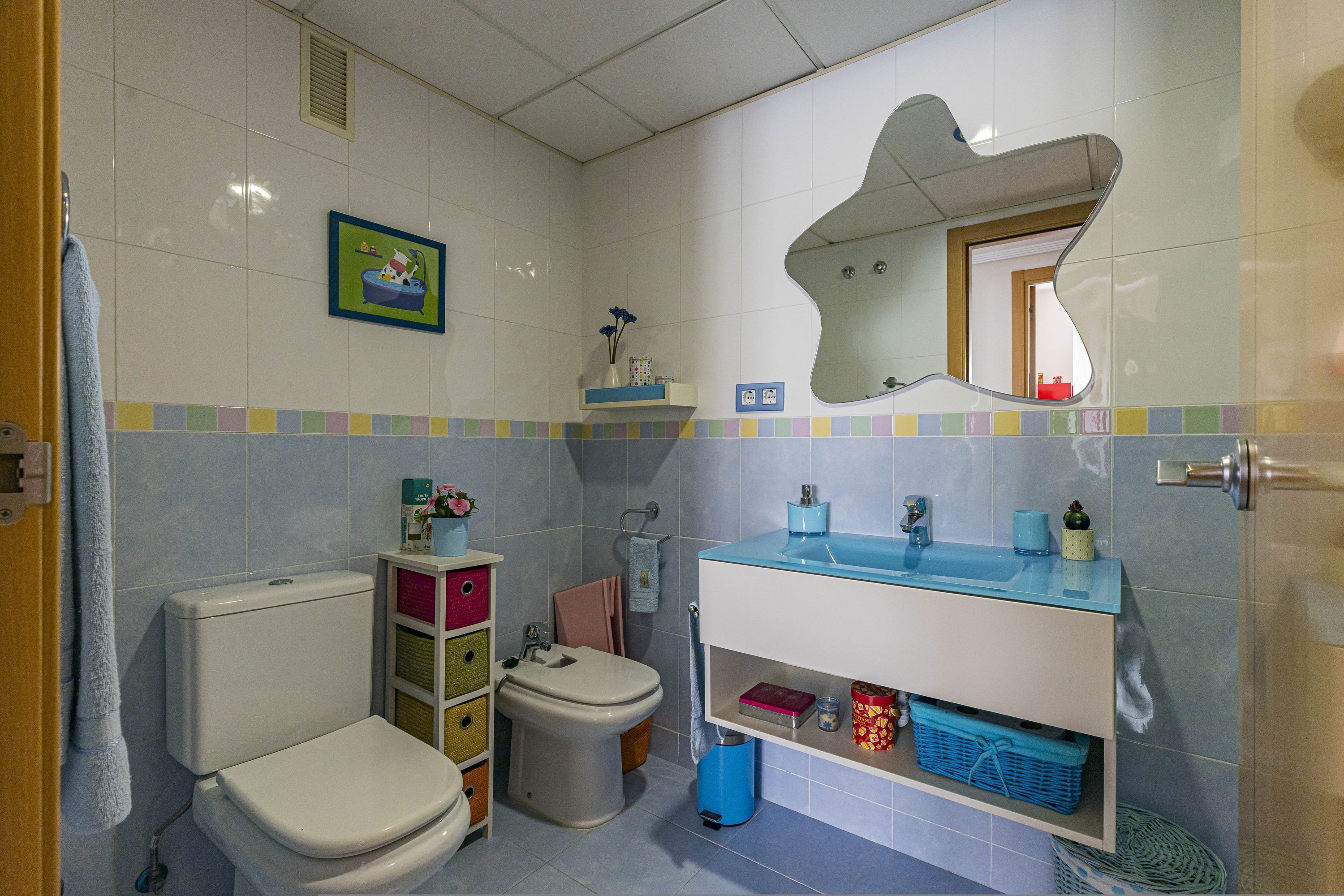 A bathroom with a toilet, bidet, and sink. There are storage shelves and a mirror.