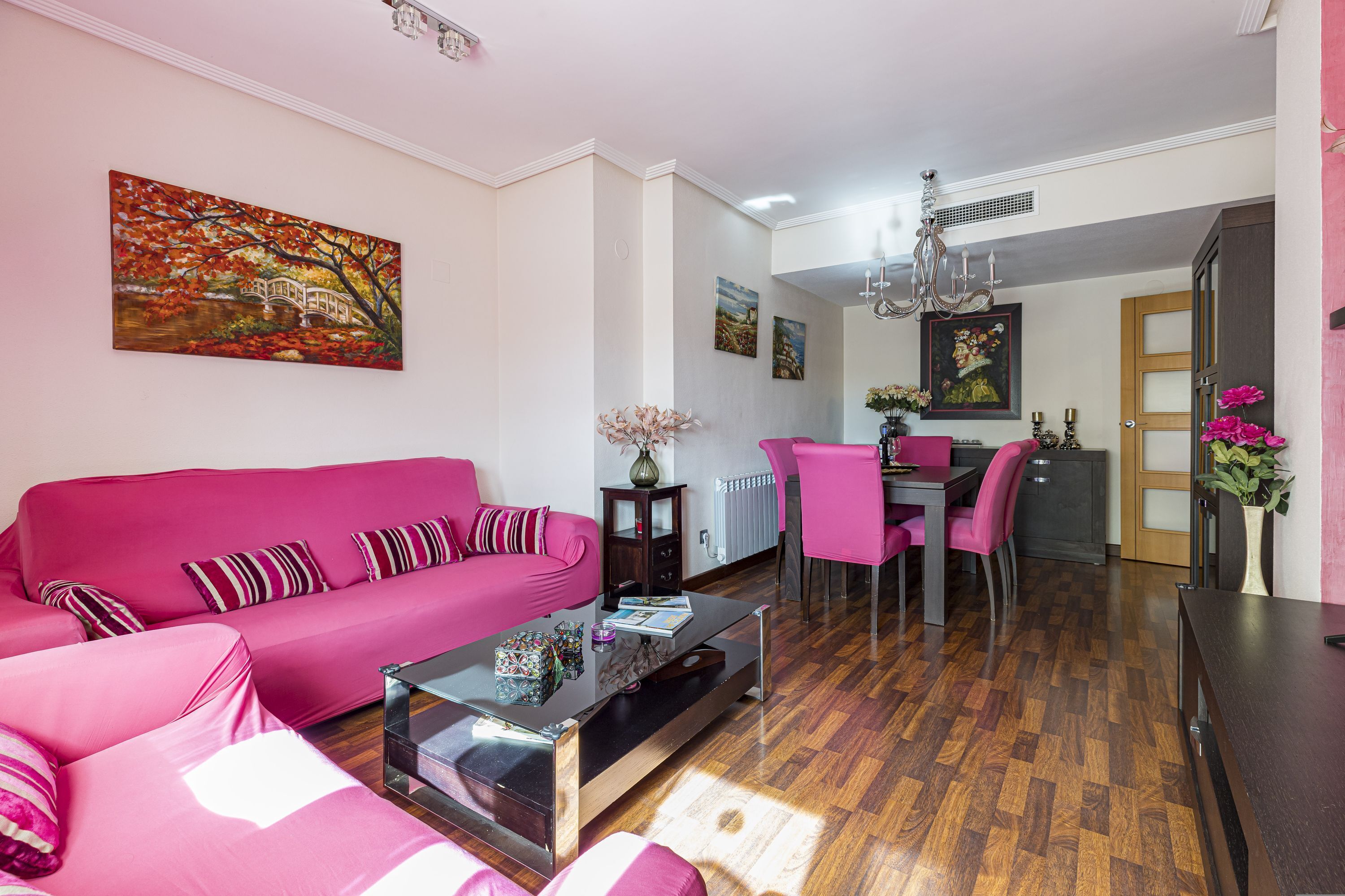 Una sala de estar moderna con un sofá rosa, una mesa de centro de vidrio y una zona de comedor con una mesa y sillas de madera.