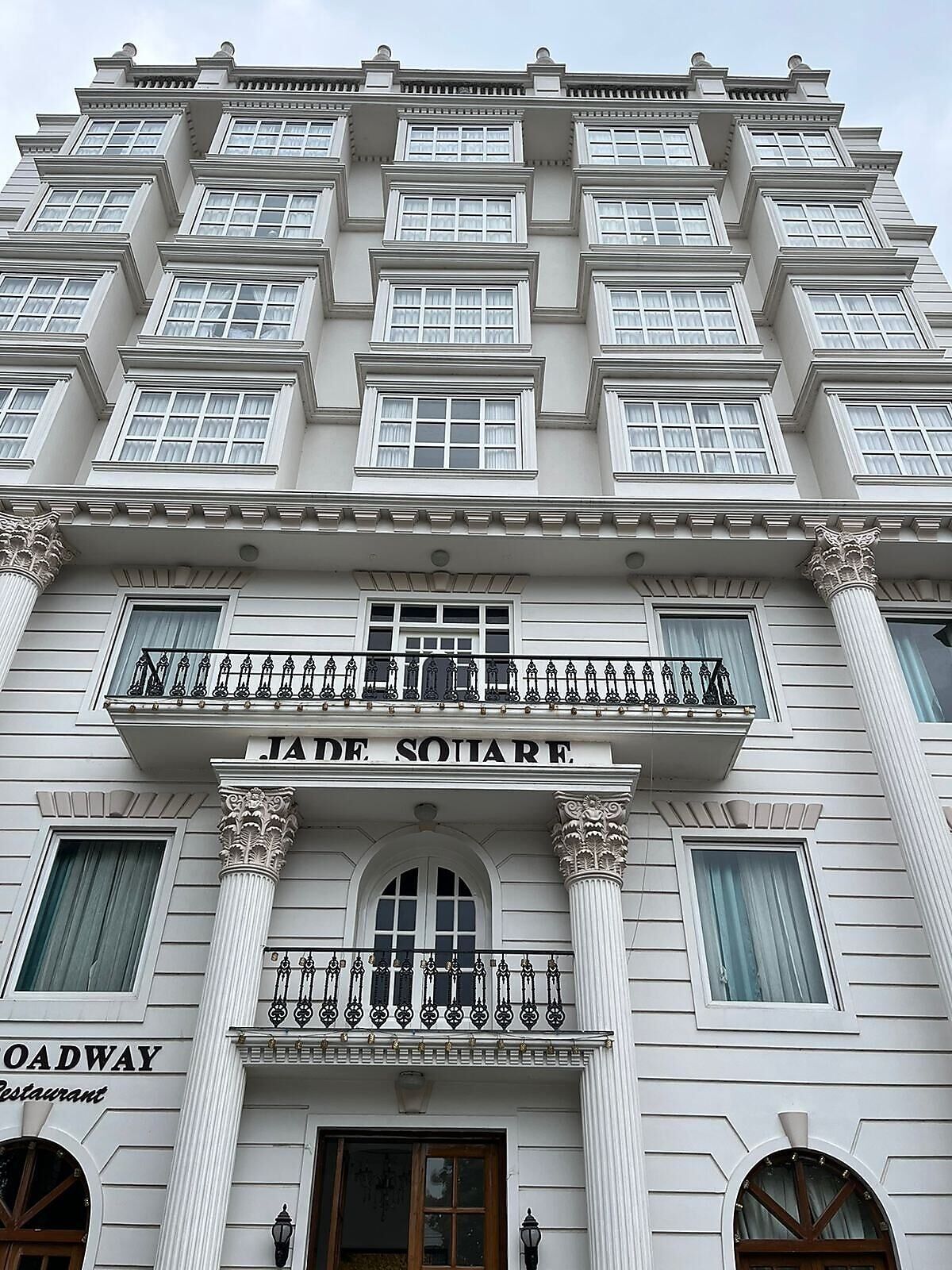 Un edificio de varios pisos con estilo arquitectónico clásico, que destaca por una entrada principal con un letrero que dice 'JADE SQUARE'.