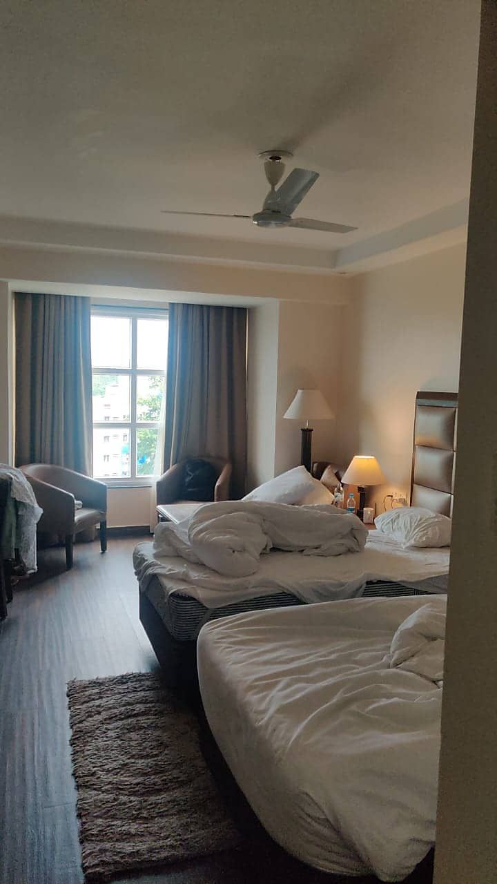 Habitación de hotel con dos camas, una silla, un escritorio, una lámpara y un ventilador de techo.