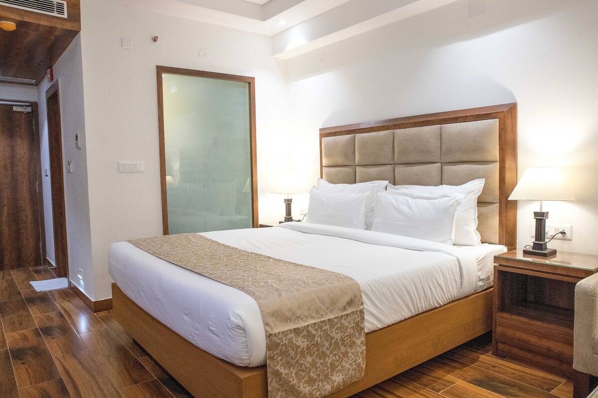 A hotel room with a large bed, wooden headboard, bedside lamps, and a wooden floor.