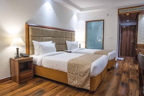 A hotel room with two beds, wooden flooring, a nightstand with a lamp, and a large mirror.
