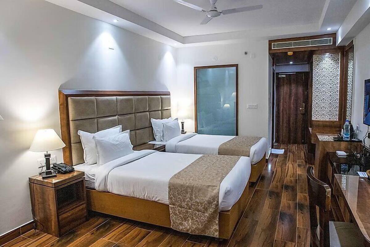A hotel room with two beds, a desk, a chair, a TV, and a ceiling fan.