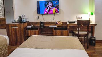 A hotel room with a bed, a desk with a television, a chair, and a trash can.