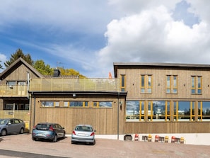 Ein modernes Gebäude mit Holzfassade, großen Fenstern und einer überdachten Außenbereich-Sitzgelegenheit.