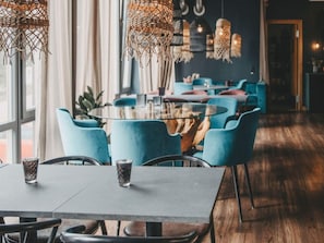 Ein modernes Interieur mit einem runden Glastisch, blauen Stühlen und hängenden Leuchten.