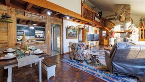 A rustic interior with a wooden dining area, a cozy seating area with patterned cushions, and a stone fireplace. - 2 Cabins on 3 Acres | Hot Tubs & Trails (Mentone)