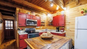 A cozy kitchen with wooden walls, red cabinets, a white refrigerator, and a wooden island with a bowl. - 2 Cabins on 3 Acres | Hot Tubs & Trails (Mentone)