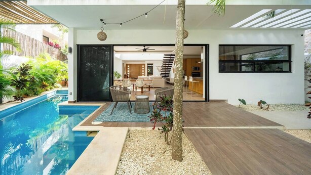 Una casa moderna con piscina, comedor y cocina visibles a través de una puerta abierta.