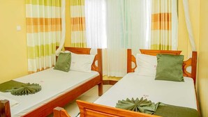 Camera d'albergo con due letti singoli, ciascuno con struttura in legno e biancheria bianca. Le pareti sono gialle e le tende a righe.