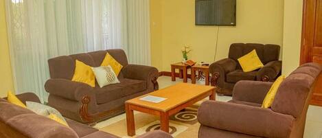 A living room with brown sofas, a wooden coffee table, and a TV on the wall.