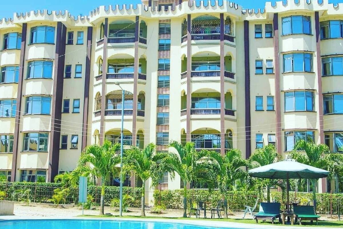 Um hotel com vários andares, varandas, piscina e palmeiras.