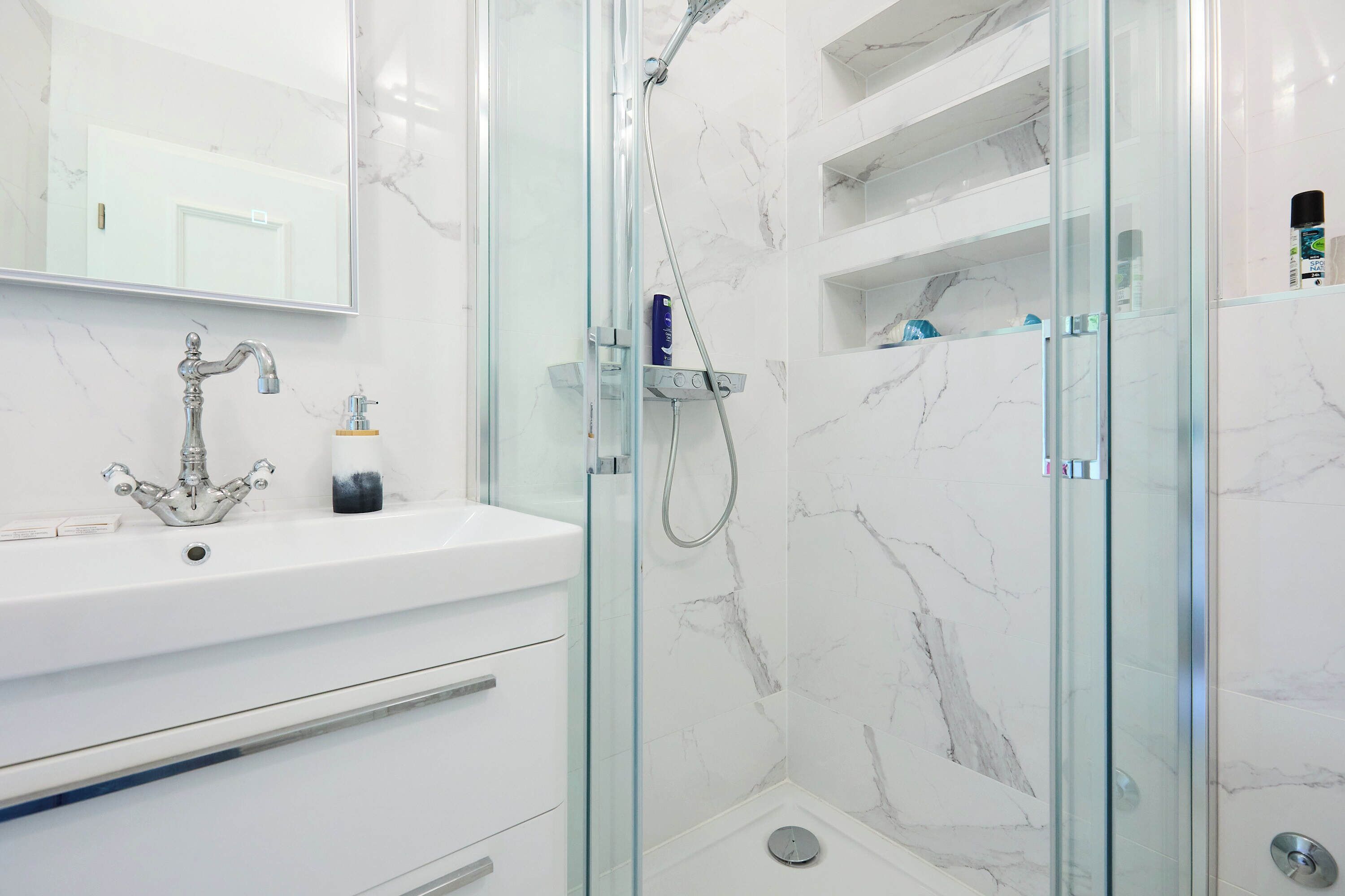A modern bathroom with a glass-enclosed shower, a white sink with a classic faucet, and marble walls.