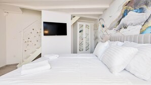 Una habitación de hotel moderna con una cama grande, un televisor de pantalla plana montado en la pared y un mural decorativo.