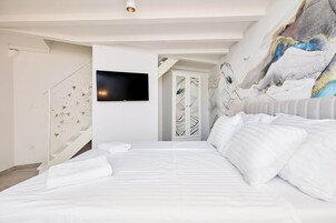 Quarto de hotel moderno com uma cama grande, televisão de tela plana na parede e um mural decorativo.