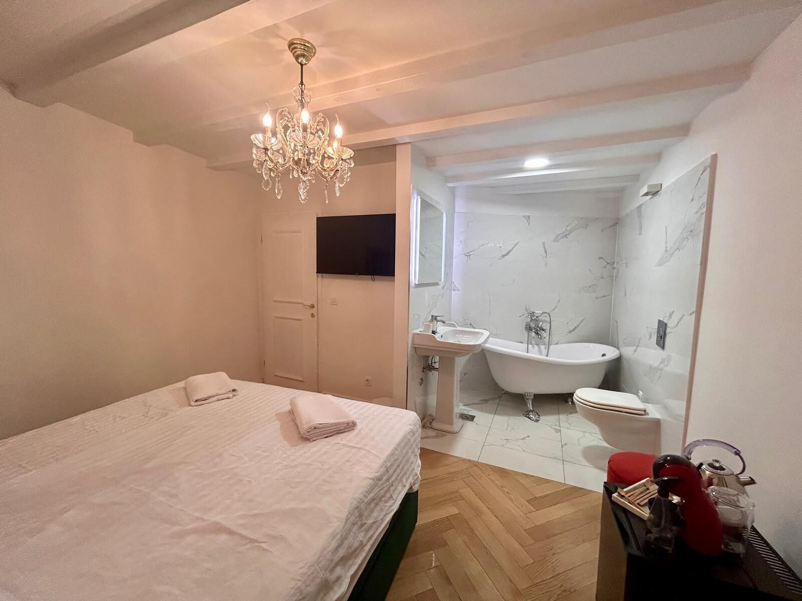 A bedroom with a bed, a chandelier, a TV, and a bathroom with a bathtub and sink.