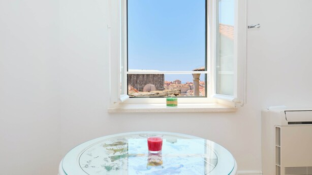 Una habitación con una mesa de vidrio, una ventana con vista a edificios y un equipo de aire acondicionado.