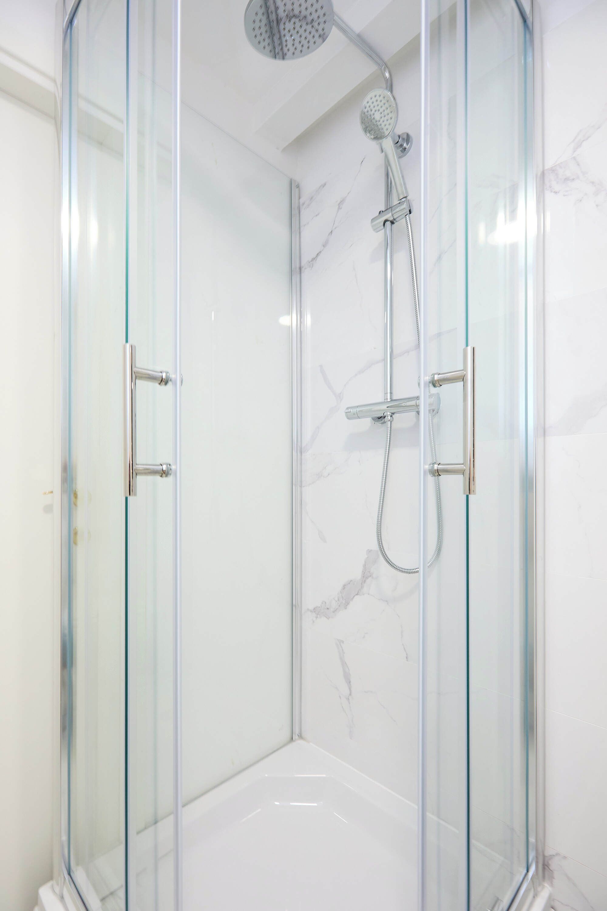 Une douche fermée par des parois en verre, dotée d’un pommeau de douche à main et d’un robinet fixé au mur.