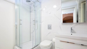 Un baño moderno con ducha envuelta en vidrio, inodoro blanco y pared de azulejos de mármol.