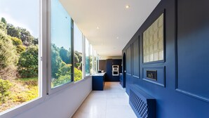 Um corredor moderno com grandes janelas, uma área de cozinha e uma parede azul escura.