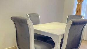 A dining table with four chairs, a white tablecloth, and a tiled floor. - Munyonyo 2bedroom Joy Apartments (Kampala)