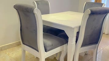 A dining table with four chairs, a white tablecloth, and a tiled floor.