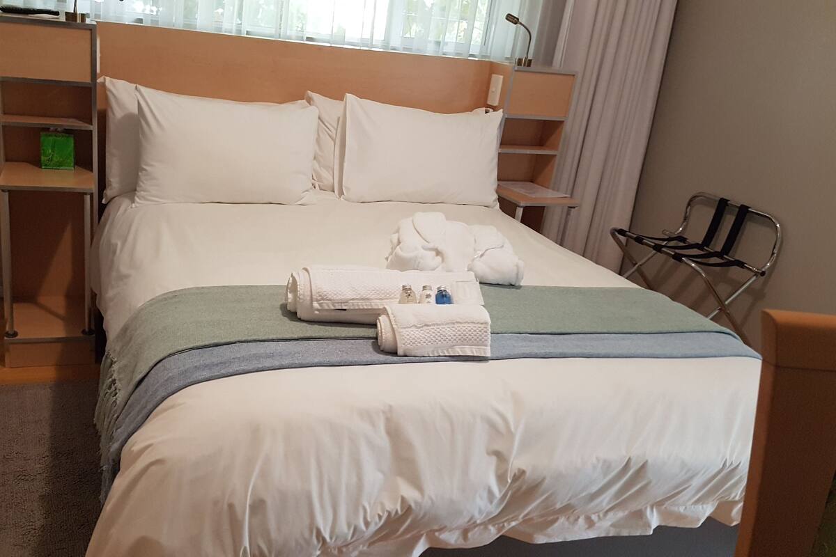 A hotel room with a large bed, a bedside table, a chair, and a window with curtains.