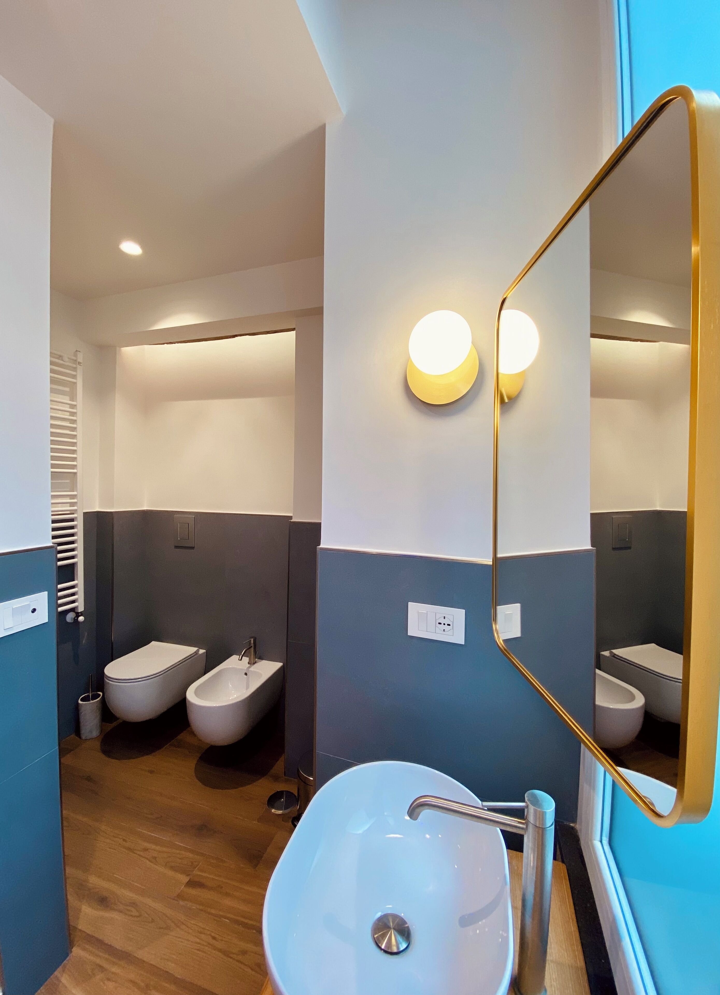 A modern bathroom with a large mirror, two urinals, a sink, and a toilet.