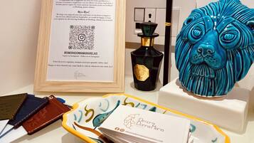 Un panneau encadré avec du texte et un code QR, une bouteille avec une étiquette, une tête de lion en céramique bleue et un plateau contenant des cartes de visite.