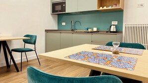 Cocina moderna con microondas, pileta y estante de madera. Hay una mesa de comedor con sillas y un camino de mesa decorativo.