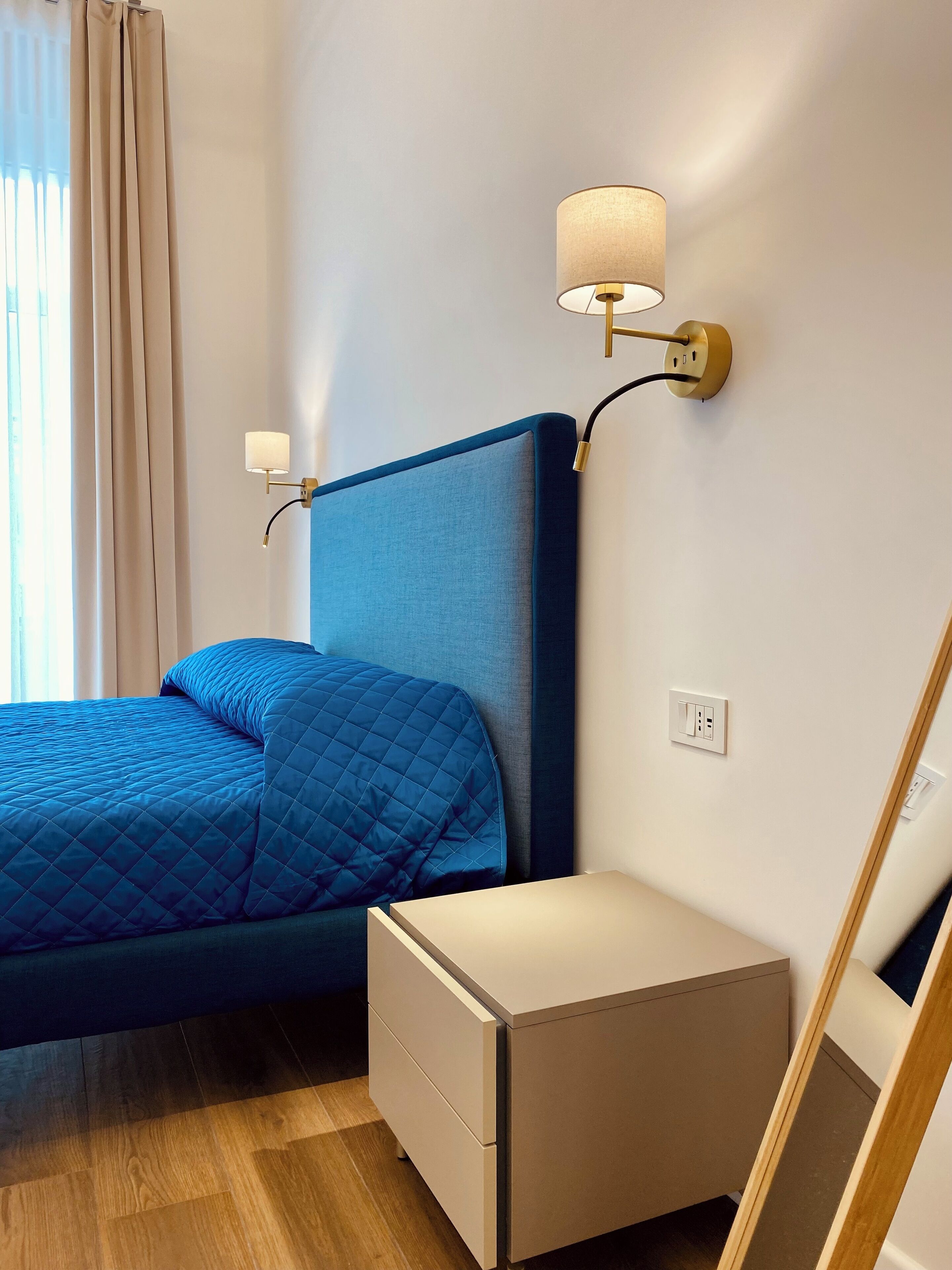 A neatly arranged hotel room with a bed, bedside table, and wall-mounted lamps.
