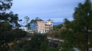 Un edificio a più piani con uno stile architettonico tradizionale, circondato da vegetazione lussureggiante e montagne sullo sfondo.