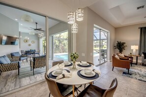 A modern dining area with a round table set for six, a glass partition, and a view of a swimming pool.