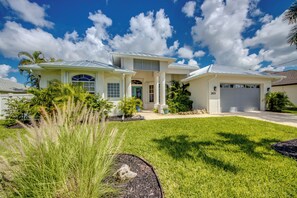 A two-story house with a garage, surrounded by well-maintained lawn and tropical plants.