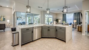 Una cocina moderna con una isla grande, electrodomésticos de acero inoxidable e iluminación colgante.