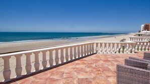 Uitzicht op het strand vanaf een balkon met een betegelde vloer en een witte balustrade.